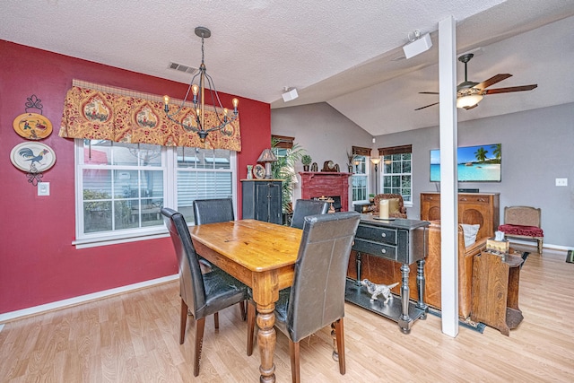 dining area featuring a textured ceiling, lofted ceiling, light hardwood / wood-style floors, ceiling fan with notable chandelier, and a brick fireplace