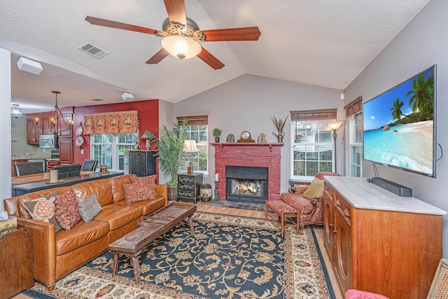 living room featuring vaulted ceiling, a textured ceiling, light hardwood / wood-style floors, and ceiling fan with notable chandelier