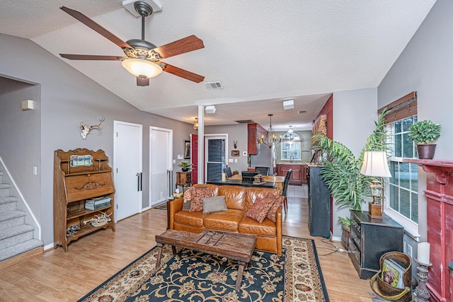 living room with ceiling fan with notable chandelier, a textured ceiling, lofted ceiling, and light hardwood / wood-style flooring