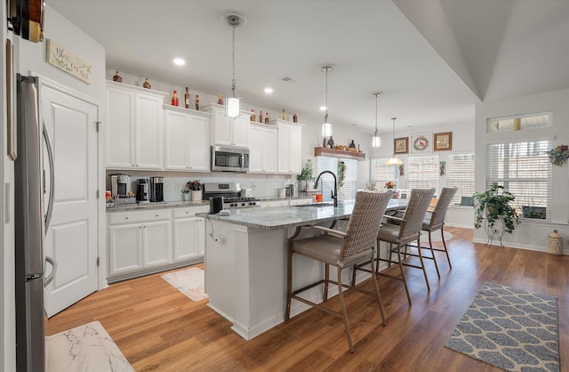 kitchen with stainless steel appliances, white cabinetry, decorative light fixtures, and a center island with sink