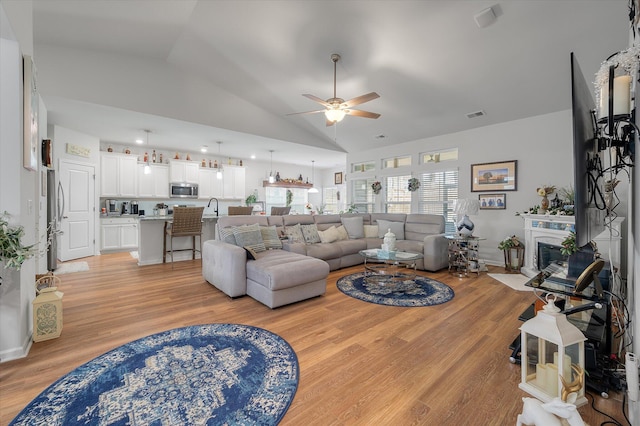 living room featuring ceiling fan, light wood-type flooring, vaulted ceiling, and sink