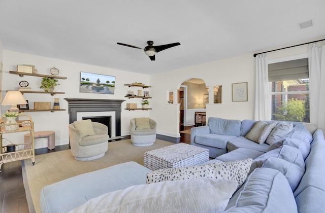 living area featuring ceiling fan, visible vents, a fireplace with flush hearth, arched walkways, and wood finished floors