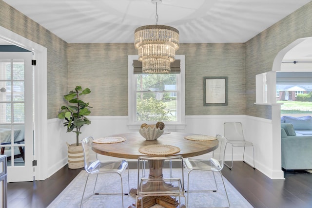 dining area featuring an inviting chandelier, wainscoting, arched walkways, wallpapered walls, and wood finished floors