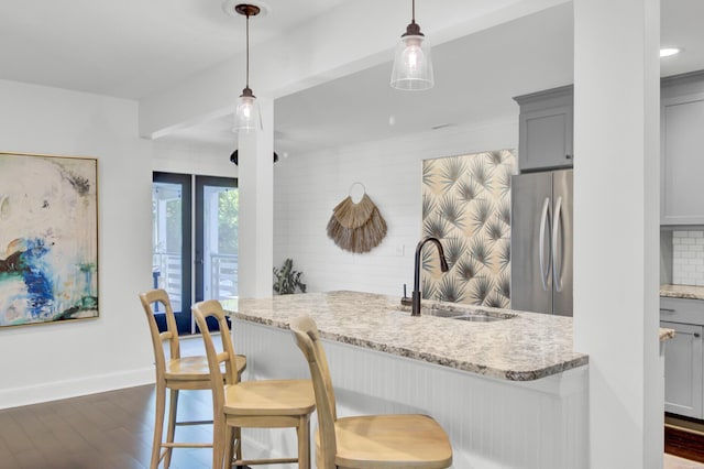 kitchen with gray cabinets, a sink, light stone counters, freestanding refrigerator, and dark wood-style floors