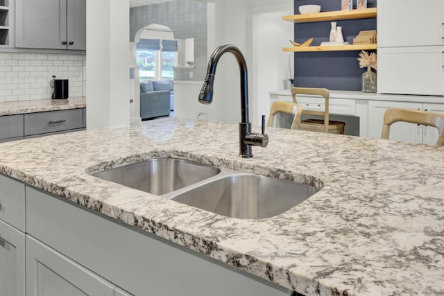 kitchen with open shelves, gray cabinets, tasteful backsplash, light stone counters, and a sink