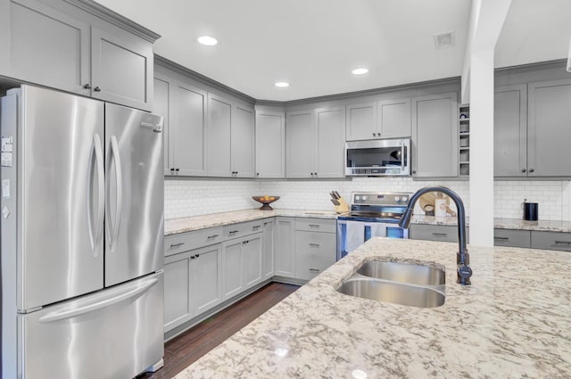 kitchen featuring appliances with stainless steel finishes, light stone counters, a sink, dark wood finished floors, and gray cabinets