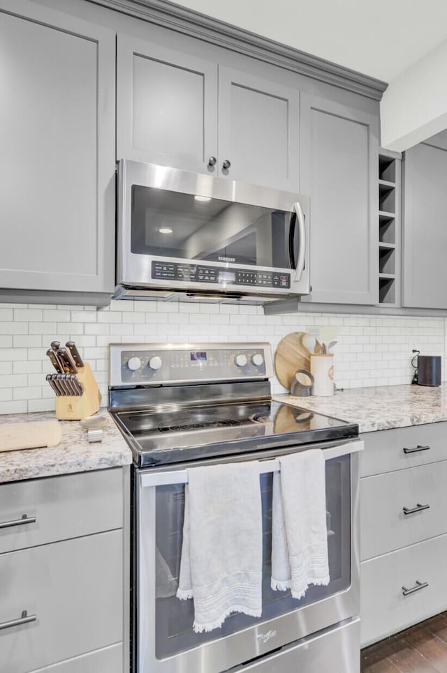 kitchen featuring appliances with stainless steel finishes, tasteful backsplash, dark wood finished floors, gray cabinetry, and light stone counters