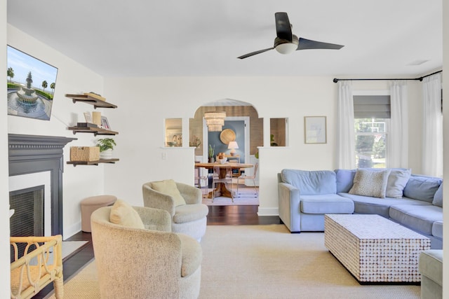 living room featuring arched walkways, ceiling fan, a fireplace with flush hearth, and wood finished floors