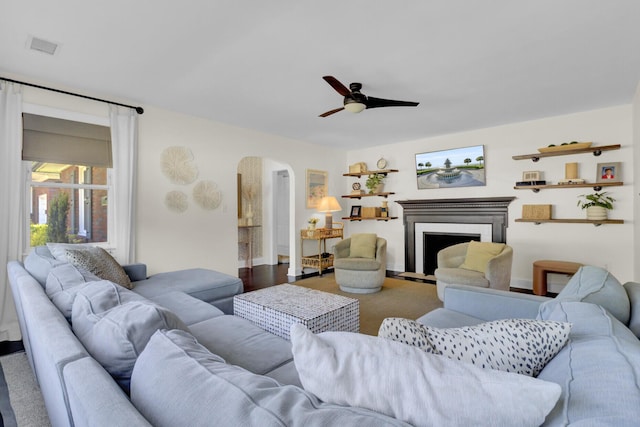 living room featuring a fireplace with flush hearth, arched walkways, and a ceiling fan