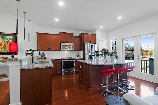 kitchen featuring a kitchen breakfast bar, stainless steel appliances, dark wood-type flooring, sink, and pendant lighting