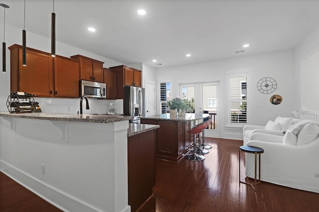 kitchen with stone countertops, dark hardwood / wood-style floors, decorative light fixtures, a kitchen bar, and stainless steel appliances