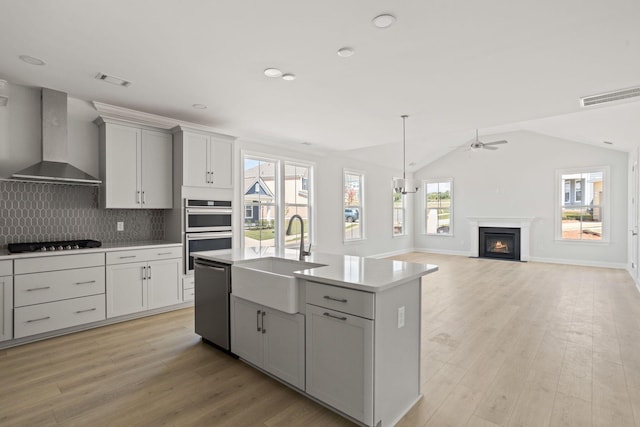 kitchen featuring stainless steel appliances, a center island with sink, sink, lofted ceiling, and wall chimney range hood