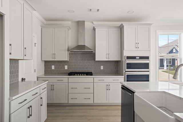 kitchen with light hardwood / wood-style floors, sink, light stone counters, appliances with stainless steel finishes, and wall chimney range hood