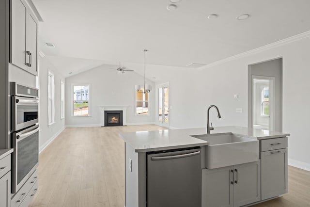 kitchen with lofted ceiling, sink, an island with sink, light wood-type flooring, and appliances with stainless steel finishes