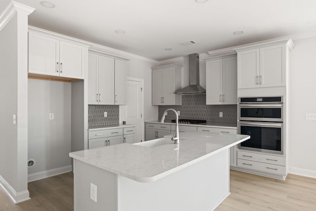 kitchen featuring wall chimney exhaust hood, a center island with sink, sink, and appliances with stainless steel finishes