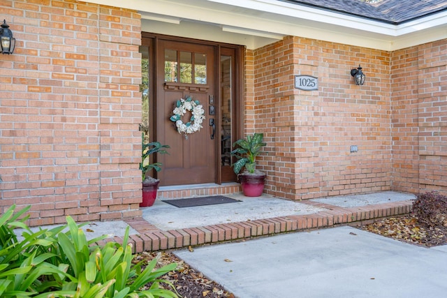 doorway to property with brick siding and a shingled roof