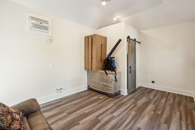 interior space with a wall mounted air conditioner, dark wood finished floors, baseboards, and a barn door