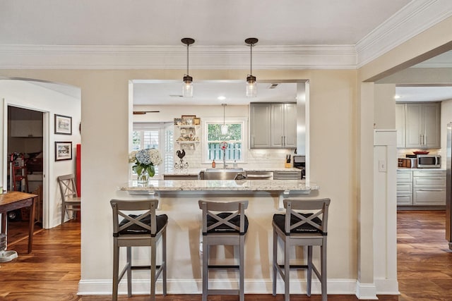 kitchen featuring arched walkways, a breakfast bar area, decorative backsplash, dark wood-style floors, and stainless steel microwave