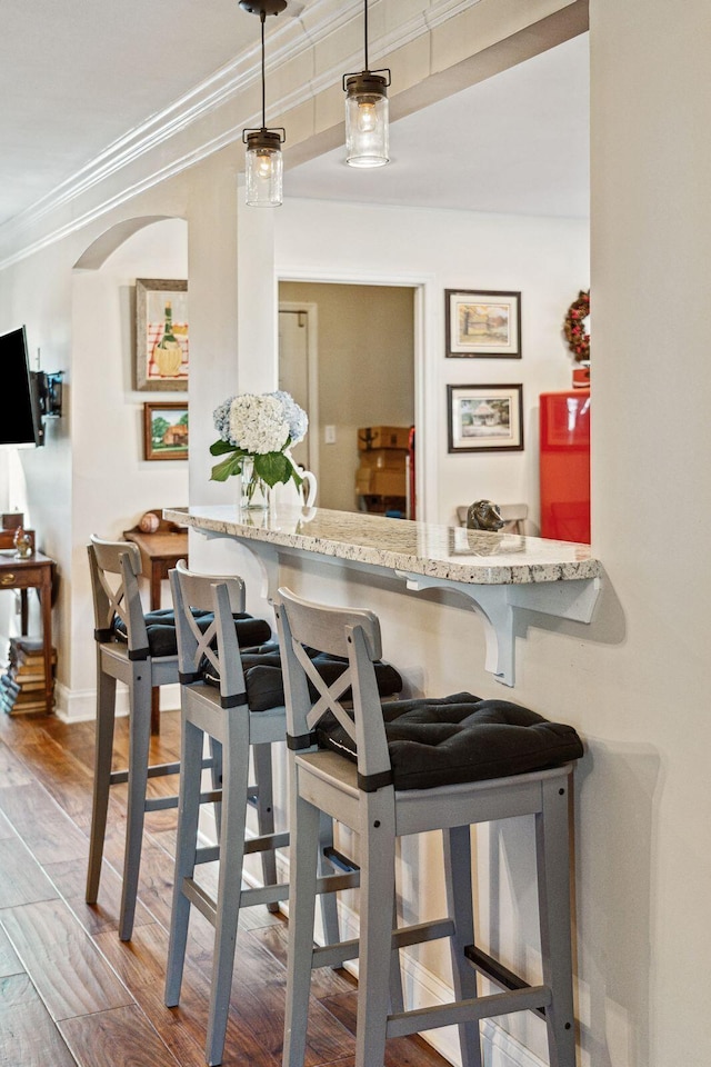 bar with baseboards, arched walkways, ornamental molding, wood finished floors, and pendant lighting