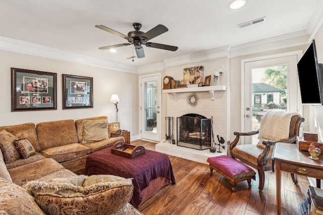 living room with visible vents, a ceiling fan, wood finished floors, crown molding, and a fireplace