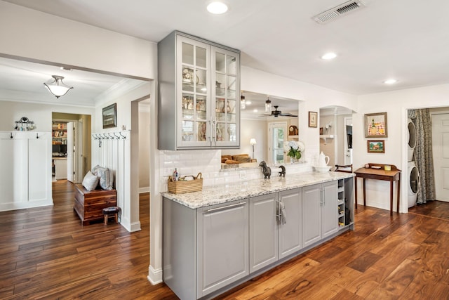 kitchen featuring visible vents, arched walkways, stacked washer / dryer, gray cabinets, and backsplash