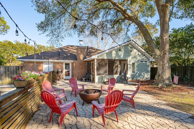 back of house featuring brick siding, a patio, an outdoor fire pit, a sunroom, and fence