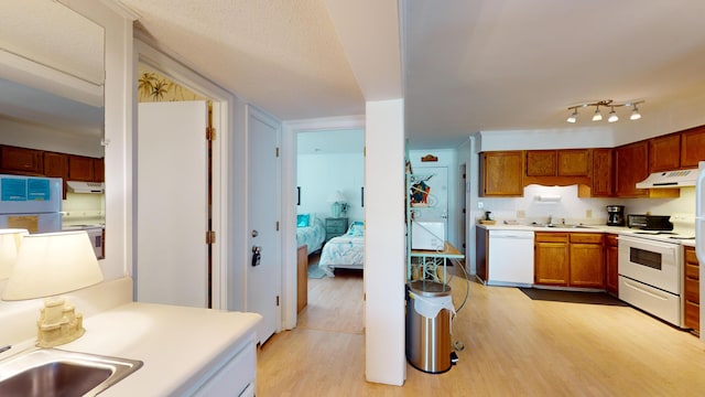 kitchen with sink, white appliances, rail lighting, and light hardwood / wood-style flooring