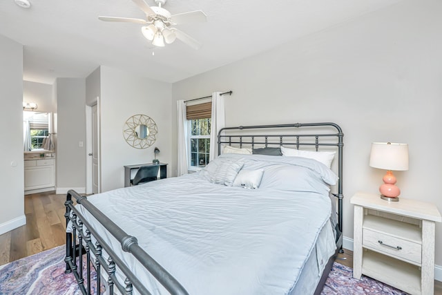 bedroom featuring a ceiling fan, ensuite bath, wood finished floors, and baseboards