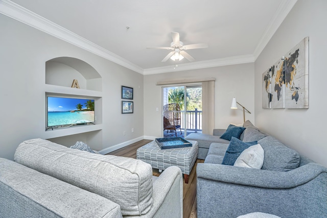 living room featuring built in shelves, crown molding, ceiling fan, baseboards, and wood finished floors