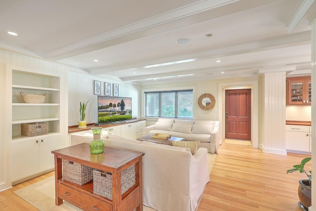 living room with built in shelves, light hardwood / wood-style flooring, ornamental molding, and beamed ceiling