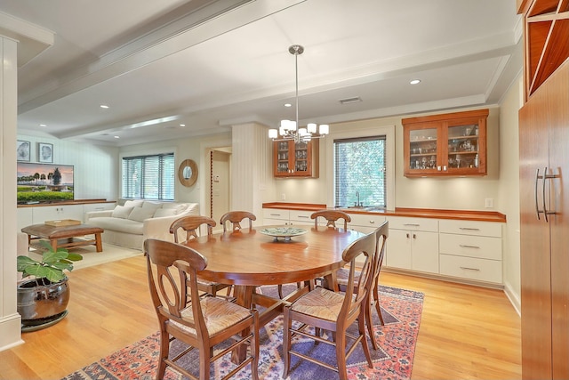 dining area featuring beam ceiling, light wood-type flooring, a notable chandelier, and crown molding