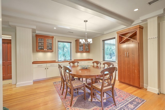 dining area with light wood-type flooring, beamed ceiling, crown molding, and a chandelier