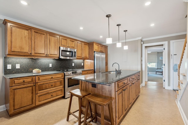 kitchen featuring an island with sink, appliances with stainless steel finishes, a kitchen bar, dark stone countertops, and sink