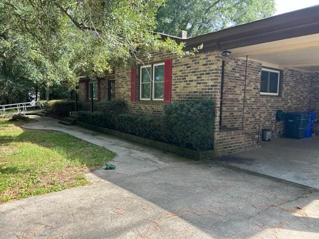 view of side of property with driveway, an attached carport, and brick siding