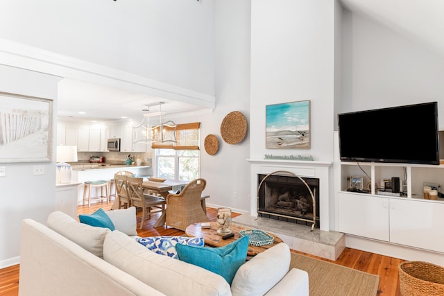 living room with baseboards, light wood-type flooring, a tile fireplace, and high vaulted ceiling