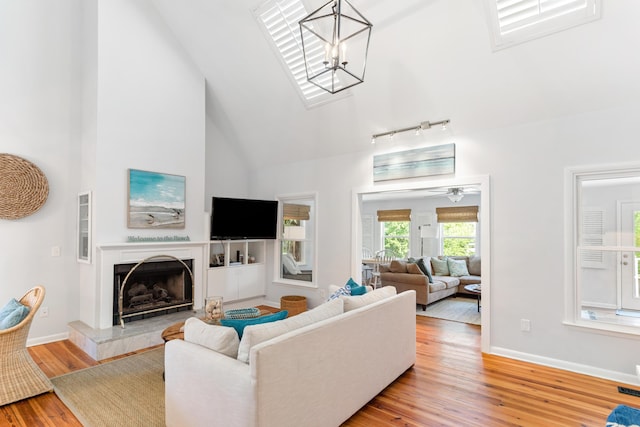 living room with track lighting, wood finished floors, a fireplace with raised hearth, baseboards, and high vaulted ceiling