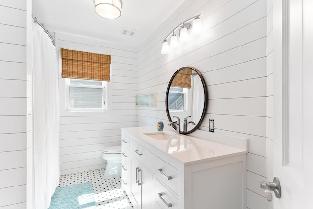 bathroom featuring tile patterned flooring, toilet, vanity, visible vents, and wooden walls