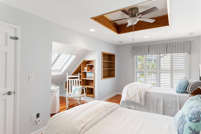 bedroom featuring baseboards, a raised ceiling, wood finished floors, and a skylight