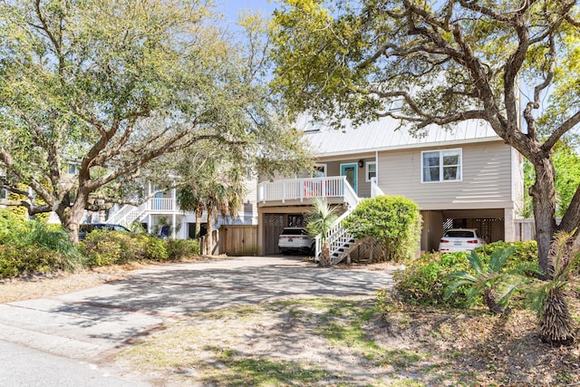 coastal inspired home featuring driveway, a carport, metal roof, stairway, and a porch