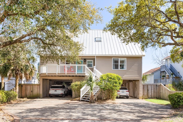 coastal inspired home with a porch, aphalt driveway, metal roof, a carport, and stairs