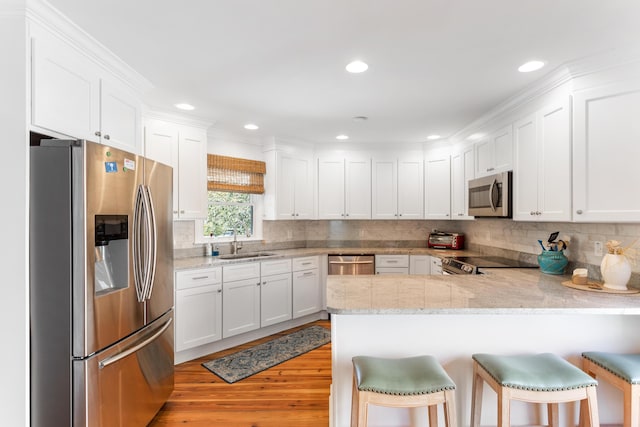 kitchen with stainless steel appliances, sink, light hardwood / wood-style floors, kitchen peninsula, and a breakfast bar