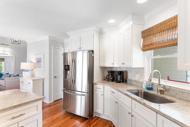 kitchen featuring stainless steel refrigerator with ice dispenser, ornamental molding, light stone counters, light hardwood / wood-style floors, and backsplash