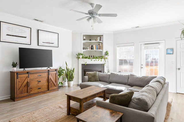 living room featuring ceiling fan, built in features, crown molding, and light hardwood / wood-style flooring