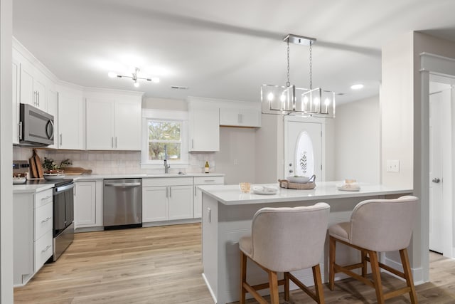 kitchen featuring white cabinets, hanging light fixtures, tasteful backsplash, a breakfast bar area, and stainless steel appliances