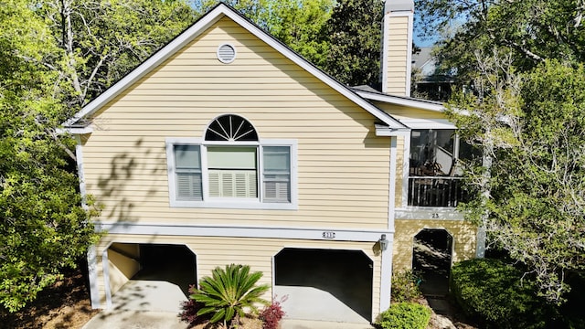 view of side of property featuring an attached garage, a chimney, concrete driveway, and a sunroom