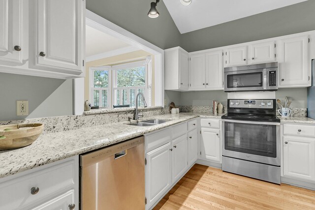 kitchen featuring appliances with stainless steel finishes, a sink, white cabinetry, light stone countertops, and lofted ceiling