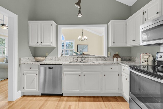 kitchen featuring appliances with stainless steel finishes, a sink, vaulted ceiling, white cabinets, and light wood finished floors