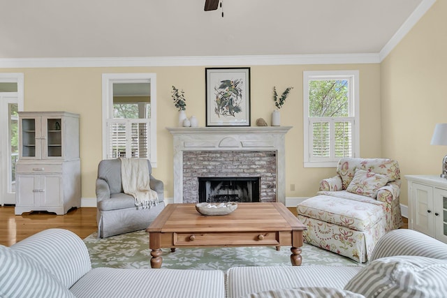 living area with crown molding, wood finished floors, a brick fireplace, ceiling fan, and baseboards