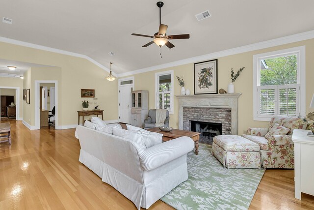 living room with light wood-type flooring, crown molding, lofted ceiling, ceiling fan, and a fireplace