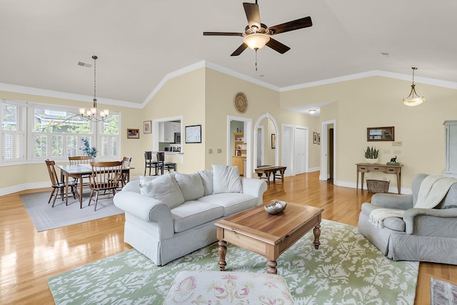 living area with vaulted ceiling, light wood-style flooring, a chandelier, ceiling fan, and arched walkways